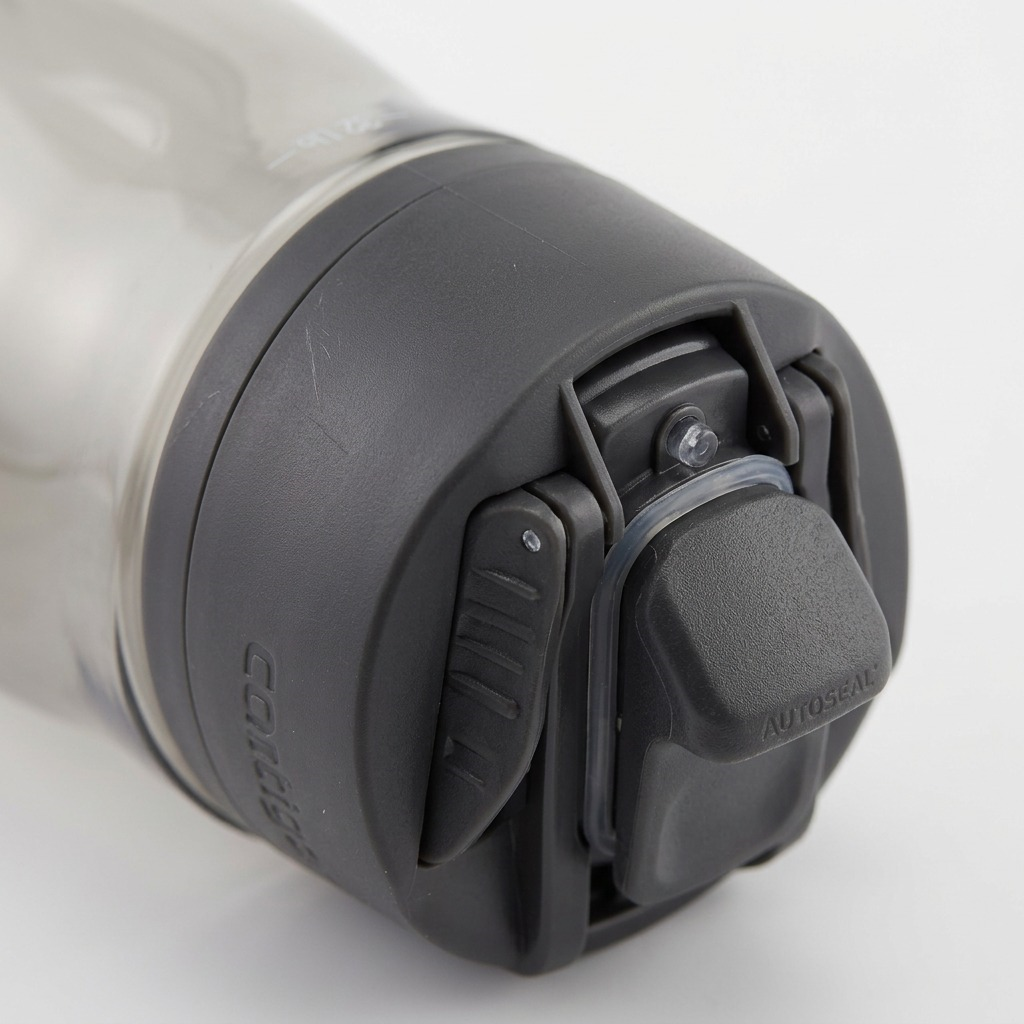 Macro detail of the dark grey Contigo AUTOSEAL lid, showing textured materials, the mechanism, and a small seal, with blurred clear bottle.